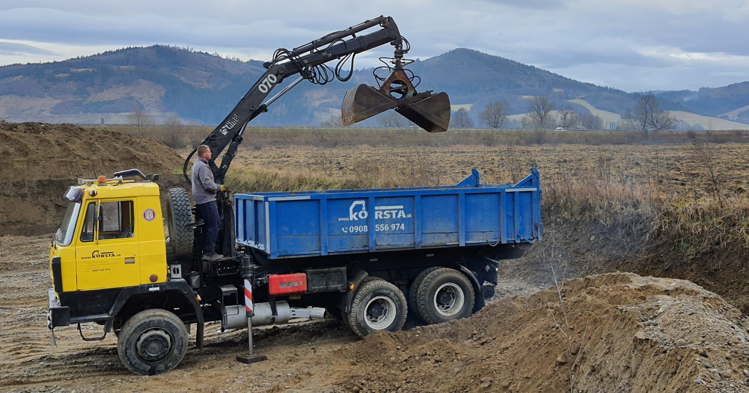 nákladné auto s hydraulickou rukou pri nakládke zeminy